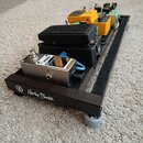 Černý pedalboard značky Harley Benton s několika efektovými pedály. V popředí je stříbrný pedal s nápisem IN u vstupního konektoru. Za ním následují…
