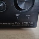 Detailní záběr na přední panel černého AV receiveru. Na spodní hraně jsou nápisy HDMI, D-R-S, dts Digital Surround, DOLBY DIGITAL PRO LOGIC II a Digi…