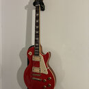 Červená elektrická kytara typu Les Paul s bílým pickguardem a dvěma humbuckery. Na hlavě je zlatý nápis „Les Paul“ a podpis „Jimmy Page“. Kytara má z…