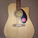 Akustická kytara s vyřezem v těle, světlým dřevem desky a tmavým hmatníkem. U rozetovém otvoru je nápis Fender CLASSIC DESIGN a na červeném samolepce…