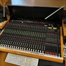 Velký míchací pult s černým povrchem a dřevěným rámem, osazený mnoha faderem a potenciometry. V pravé horní části je vidět nápis "Soundcraft" a model…