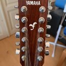 Hlava akustické kytary z tmavého dřeva s dvanácti ladicími kolíky v chromovém provedení. V horní části je bílý nápis YAMAHA a uprostřed se nachází bí…