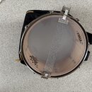 Fotografie zobrazuje snare drum s průhlednou membránou a kovovým obručím. Na membráně je viditelné logo REMO s nápisem "AMBASSADOR" a na korpusu je n…