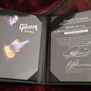 Rozložený černý certifikát pravosti s nápisem GIBSON CUSTOM CERTIFICATE OF AUTHENTICITY. Dokument obsahuje text INSPIRED BY SERIES JOE BONAMASSA AGED…