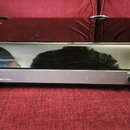Šedý gramofon s černým lesklým krytem. Na přední straně je nápis VESLA HC 470 HIFI TURNTABLE a přepínač s označením STOP LIFT a PLAY. Zařízení má pří…