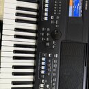 Černý digitální klavír značky YAMAHA s bílými a černými klávesami. Na ovládacím panelu je displej s modrým podsvícením, několik řad tlačítek a ovláda…