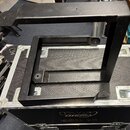Černý kovový rám v podobě dvou obdélníkových konstrukcí, jedna v druhé. Rám je položen na transportním kufru s nápisem KV audio BSD 12. Povrch rámu v…