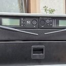 Černý rack s dvěma rádiovými přijímači a spodním panelem. Na horních zařízeních jsou viditelné displeje, ovládací prvky a logo s písmenem S v čtverci…