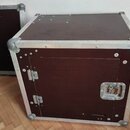 Hnědý transportní kufr s kovovými hranami a rohovými zpevněními. Na přední straně je vidět přívratný zámek a dvě panty u dveřiček. Povrch vykazuje dr…