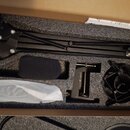 V černé pěnové výplni krabice je umístěn černý mikrofonní rameno s pružinou, pop필trovací clona (windshield) a mikrofonní shock mount. V horní části j…