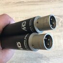 Dvě černé válcové součástky s kovovými konektory na koncích. Na tělech je bílé logo MG a nápisy GEFELL GMBH, MADE IN GERMANY. Na kovových částech je…