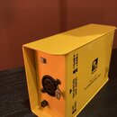 Žlutý kovový box s nápisem Palmer DACCAPO re-amplification box. Na zadní straně je jeden XLR konektor, dva přepínače a nápisy BALANCED LINE INPUT, LI…