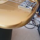 Detail zlaté elektrické basy s kovovým mostem a dvěma ovládacími knoflíky. Na mostu je vyryt nápis "Gotoh". Na spodní hraně těla nástroje je viditeln…