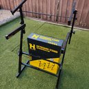Černý kovový stojan na klávesy s teleskopickými rameny. V konstrukci je umístěna žlutý a černý papírový obal s nápisy HERCULES, KEYBOARD STAND KS400B…