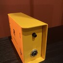 Žlutý kovový box s pravým bočním panelem, který obsahuje jeden černý otočný knoflík a jeden konektor. Na horní hraně je nápis LEVEL, pod ním se nachá…