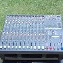 Šedý mixážní pult s mnoha posuvníky a ovládacími knoflíky. V pravé horní části je viditelné logo YAMAHA. Zařízení je umístěno venku na tmavém povrchu…