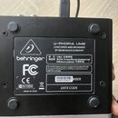 Zadní strana černého audio rozhraní s bílým štítkem. Na štítku je logo a nápis behringer, model U-PHORIA UM2 a text CONCEIVED AND DESIGNED BY BEHRING…