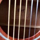 Fotografie zachycená skrze otvory v těle akustické kytary zobrazuje vnitřní štít. Na štítu je logo Cort GUITARS, označení MODEL: A150M OP a SERIAL NO…