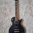 Černá elektrická kytara s tvarem single-cutaway a hnědým hmatníkem. Na hlavě je bílý nápis Lizmaud. Kytara má dva humbuckery, čtyři ovládací knoflíky…
