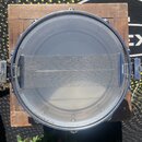 Fotografie zachycuje pohled shora do vnitřku kovového bubnu s napnutou průhlednou blánou. Uprostřed je umístěna kovová síťka s dvěma bočními úchytky.…