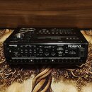 Zadní strana černého elektronického bicího modulu značky Roland. Jsou zde viditelné různé výstupní a vstupní konektory, včetně USB portu s nápisem US…