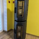 Dvě černé aktivní reproduktory značky the box pro speakers, které jsou naskládány na sebe. Na zadním panelu každého reproduktoru je zlatý kovový prve…