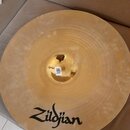 Zlatavý kovový činel s viditelným opracováním povrchu v koncentrických kruzích. Ve spodní části je černý nápis Zildjian. V centru cinchlu je nalepená…