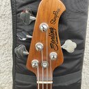 Hlava basové kytary z dřeva s viditelnou masivní strukturou. Na povrchu je žlutý nápis Sterling by MUSIC MAN StingRay®. Jsou zde čtyři chromované lad…