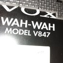 Detailní záběr na černý efekt pedál s gumovou texturou v horní části. Na povrchu je bílý nápis VOX WAH-WAH MODEL V847. Ve spodní části je vidět bílá…