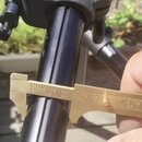 Fotografie zachicuje detail černé kovové nohy stativu. Průměr trubky je změřován posuvným měridlem, které ukazuje hodnotu přibližně 25 mm. Na povrchu…