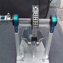 Stříbrný kovový stojan s modrými doplňky, na kterém je upevněn řetězový mechanismus. V pozadí je černá přepravní taška s bílým logem Yamaha. Na spodn…