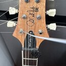 Hlava dřevěné kytary s bílými ladičkami. Na hlavě je černý nápis SE a podpis Paul Reed Smith SM®. Na hrazdici je viditelný nápis McCarty 59 a vložky…