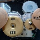 Sada cymbálů a bubnů v bílém provedení. Na cymbálech jsou viditelné nápisy Paiste pst 5 a MEINL s logem v podobě stylizedovaného písmene B. Na bubnec…