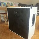 Zadní strana bílého reproduktorového boxu s černým povrchem v zadní části. V horní části je umístěn panel se dvěma konektory a přepínacím spínáčem. B…