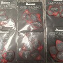 Šest uzavřených balení kytarových trsátek. Na každém černém obalu je bílý nápis Ibanez GRIP WIZARD MADE IN JAPAN. Uvnitř každého balení jsou šedé trs…