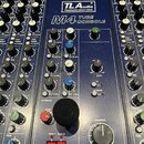 Modrá mixovací konzole s nápisy TLA audio, Passionate about tubes a M4 TUBE CONSOLE. V horní části jsou dvě analogové VU metry. Panel obsahuje množst…