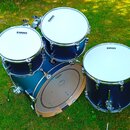 Sada tmavě modrých bubnů s bílými blány, na kterých je vidět nápis EVANS. Sestava obsahuje basový buben, dva tom-tomy a jeden floor tom s kovovými ob…