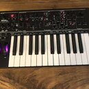 Černý syntetizátor s klaviaturaí a ovládacími prvky v horní části. Na levé straně je nápis NOVATION AFTERTOUCH XL. Přístroj obsahuje početné otočné k…