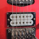 Detail červené elektro kytary s dvěma snímači. Spodní humbucker je stříbrný a nese nápis Seymour Duncan, je osazen v černém rámečku. Pod snímačem je…
