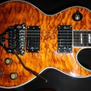 Elektrická kytara s tělem v oranžovém plamenovém provedení a bílým lemováním. Nástroj má dva humbuckery, čtyři otočné knofíky a přepínač s nápisem TR…