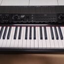 Černý digitální klavír s bílými a černými klávesami. Na ovládacím panelu jsou nápisy MASTER VOLUME, DYNAMICS, EQUALIZER, TREMBLE a FAVORITE. Jsou zde…