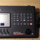 Černý elektronický modul s displejem a ovládacími tlačítky. Na horní straně je bílý nápis YAMAHA a v dolní části označení DTX Version 2.0 DRUM TRIGGE…