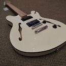 Bílá polodublová elektrická kytara s f-otvory a hnědým hmatníkem. Nástroj má dva humbuckery, dva ovládací knofíky a přepínač. Na kytáře nejsou vidite…
