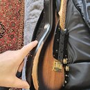 Elektrická kytara s tělem v tmavě hnědém sunburst provedení a černým pickguardem. Na hraně těla je viditelné výrazné opotřebení laku a odřeniny, kter…