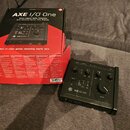Černý audio rozhraní AXE I/O One v originálním balení. Na zařízení i na krabici je viditelné logo Luthier a nápis AXE I/O ONE. Přístroj má několik ov…