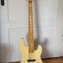 Světle béžová elektrická basová kytara s přírodním dřevěným hnedem krku a hmatníkem. Na hlavě je viditelné logo "Squier". Tělo nástroje má dva snímač…
