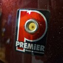 Detailní záběr na červený lakovaný povrch nástroje s nalepenou černobílou nálepkou. Na nálepce je červené písmeno P a pod ním bílý nápis PREMIER a MA…
