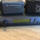 Na fotografii je modrý bezdrátový přijímač s nápisem TRUE DIVERSITY RECEIVER GW 500 G2 a logem SENNHEISER. Na něm leží modrý vysílač s nápisem SENNHE…