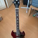 Elektrická kytara s tmavě červeným bodies a černou hlavou. Na hlavě je bílé logo ve tvaru kosočtverce a nápis Philips GUITARS. Hmatník má trojúhelník…