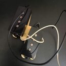 Dvě elektrické kytarové snímače typu humbucker s černými plastovými kryty a viditelnými polkovými magnety. Snímače jsou umístěny na světlém dřevěném…